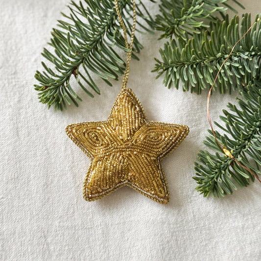 Gold star ornament hanging on a branch with a white background