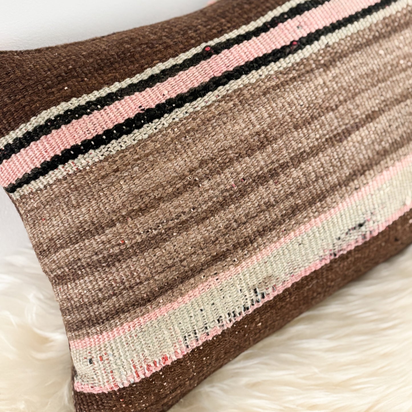 Textured pillow with brown, pink, and black stripes on a white background
