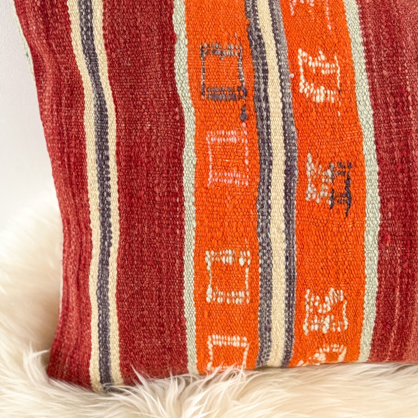 Textile pillow with red, orange, and white stripes on a white background