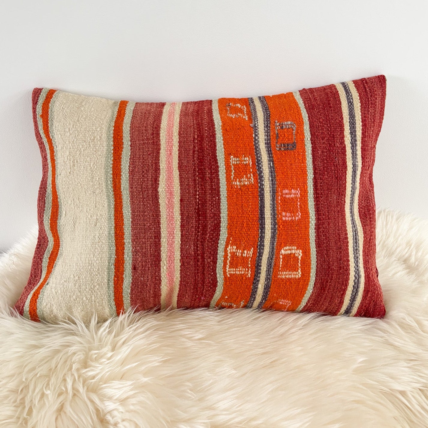 Striped pillow with red, orange, and beige colors on a white furry surface.